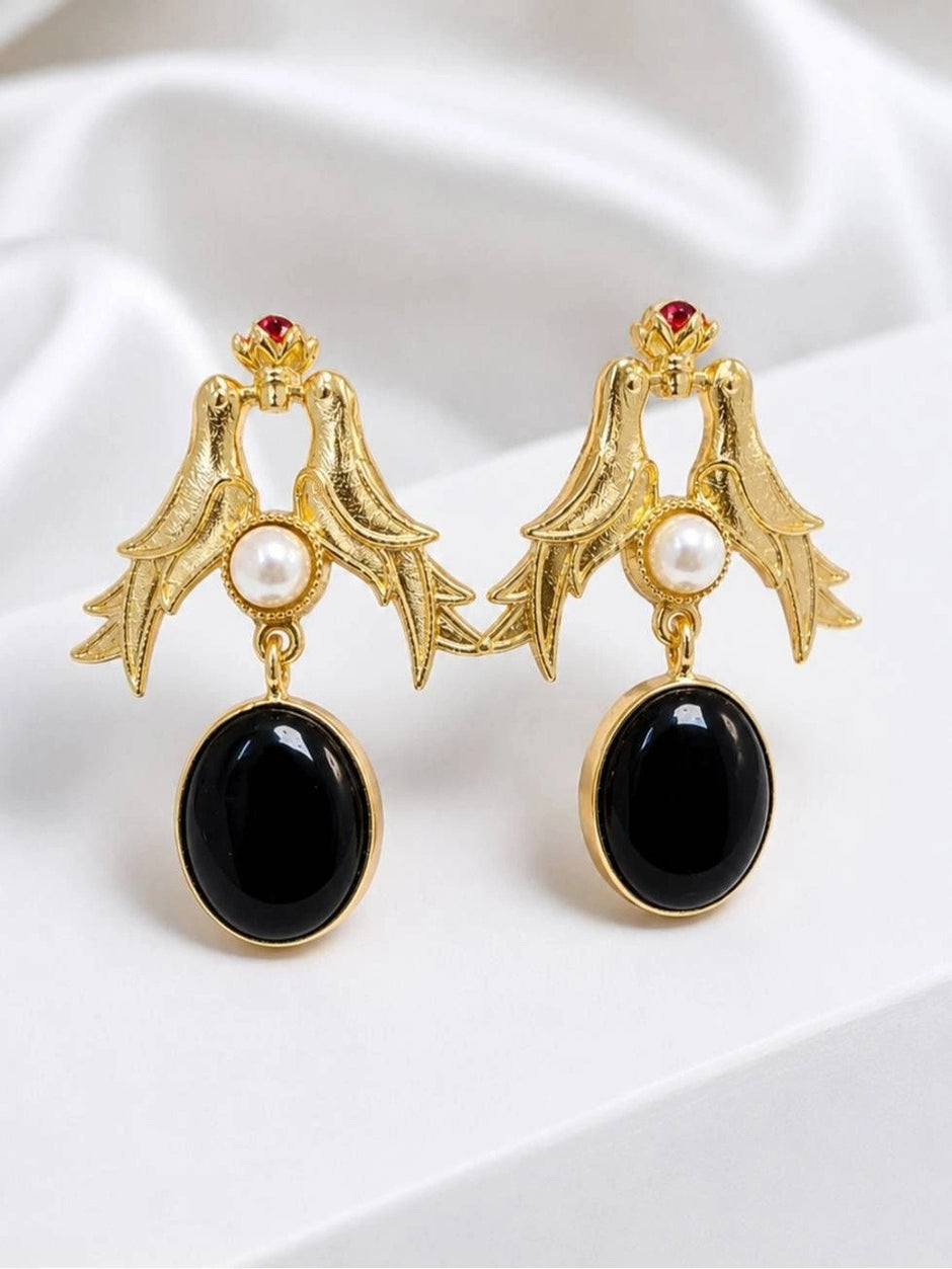 Pair of gold-plated twin swallow bird drop earrings with pearl centre and black oval pendant on white fabric