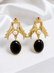 Pair of gold-plated twin swallow bird drop earrings with pearl centre and black oval pendant on white fabric