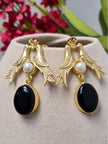 Both gold bird drop earrings displayed on a beige jewellery cushion with pink flowers in background