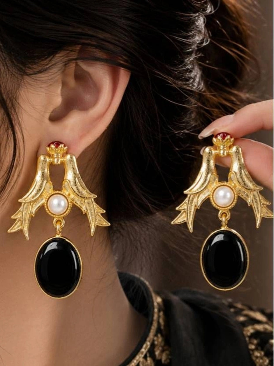 Gold bird drop earring worn on a woman's ear alongside the second earring held in hand