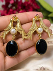 Close-up of gold swallow bird earrings with black oval drop and red stone crown detail held in palm