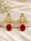 Pair of gold-plated love birds drop earrings with red oval stone and pearl on a smooth stone surface