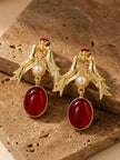 Close-up of gold love birds earrings with faux pearl centre and deep-red drop stone on textured travertine