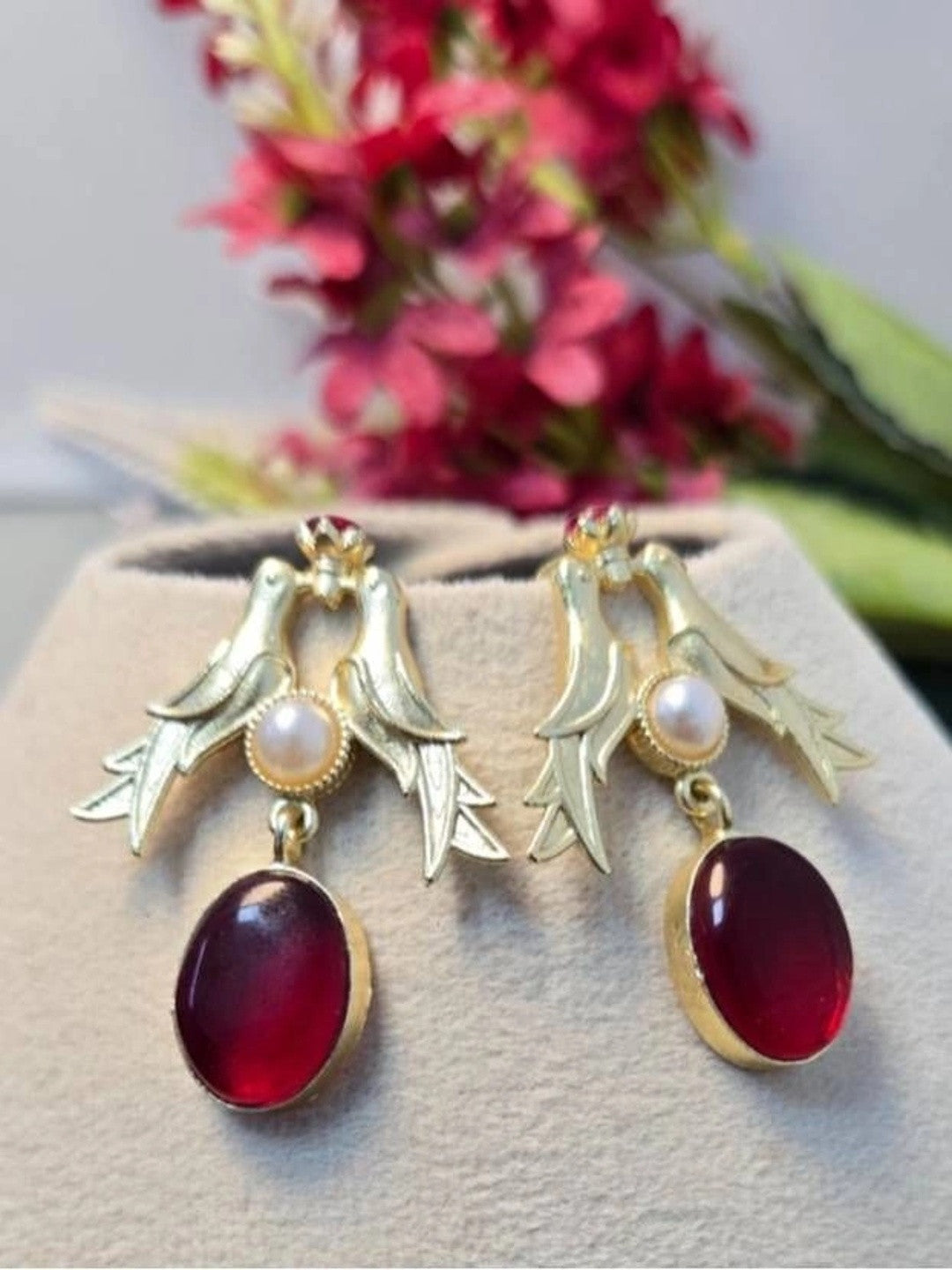 Both gold bird drop earrings displayed upright on a jewellery cushion with pink floral background