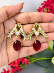 Gold love birds drop earrings held in an open palm showing full scale and red oval stone detail