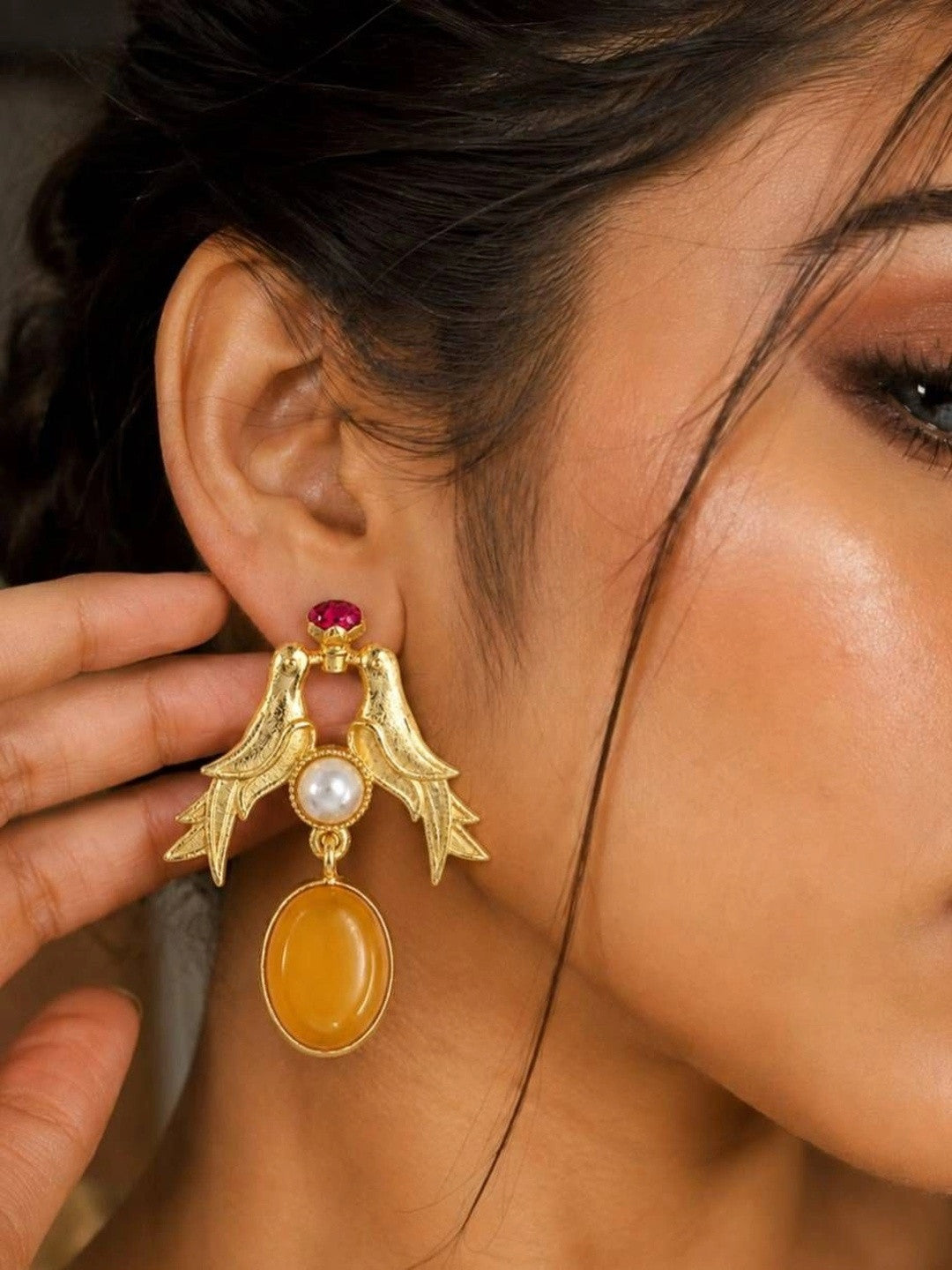 Model wearing gold-plated love birds earring with amber resin drop close up on ear