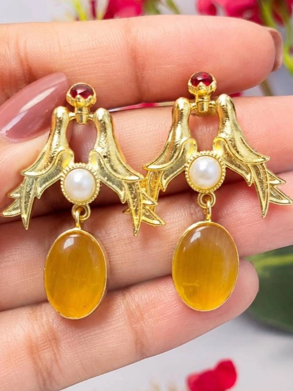 Two gold-plated love birds drop earrings with faux pearl and amber drop held in palm