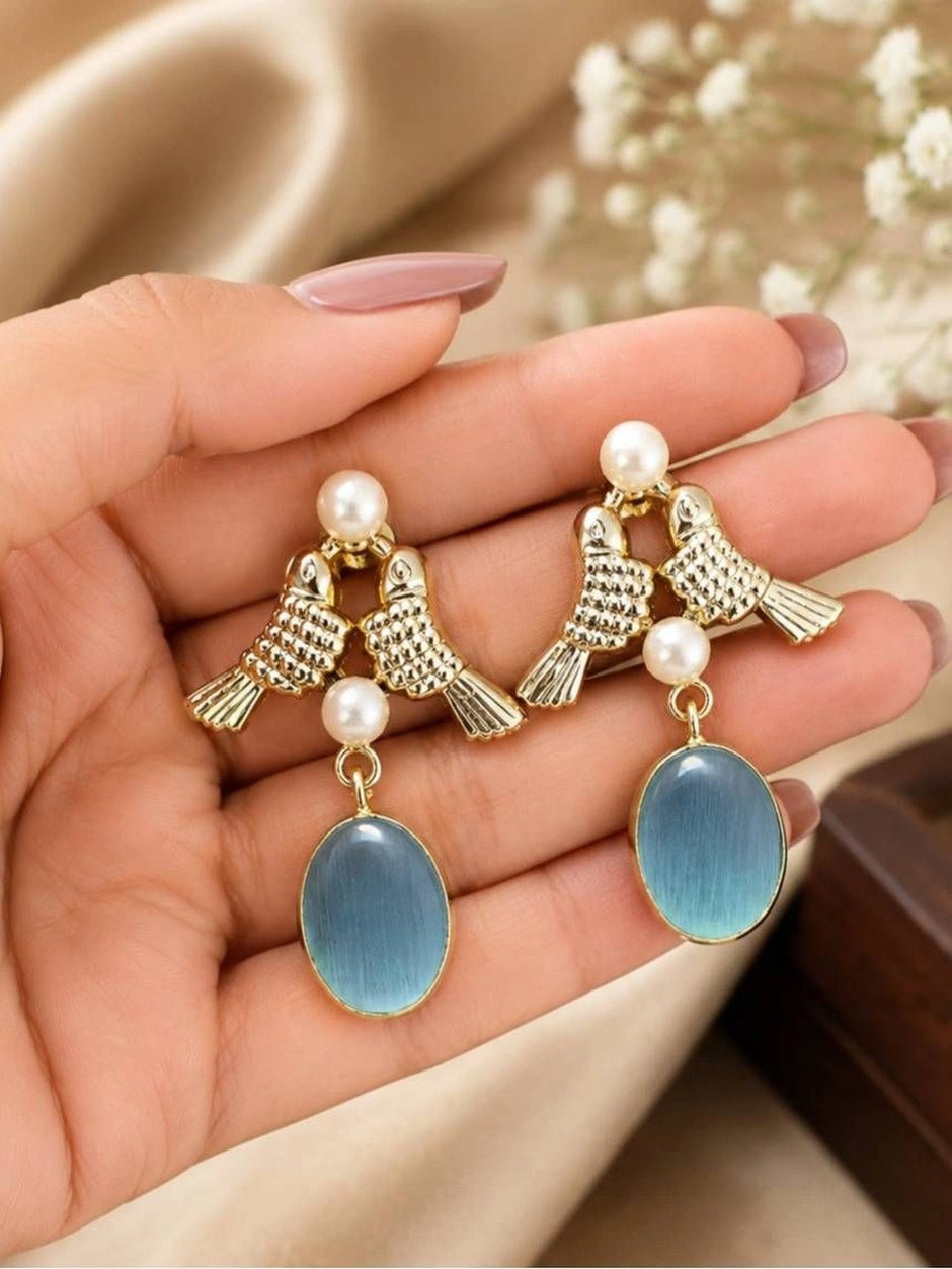 Gold lovebird earrings with faux pearls and blue oval drop held in a woman's open palm