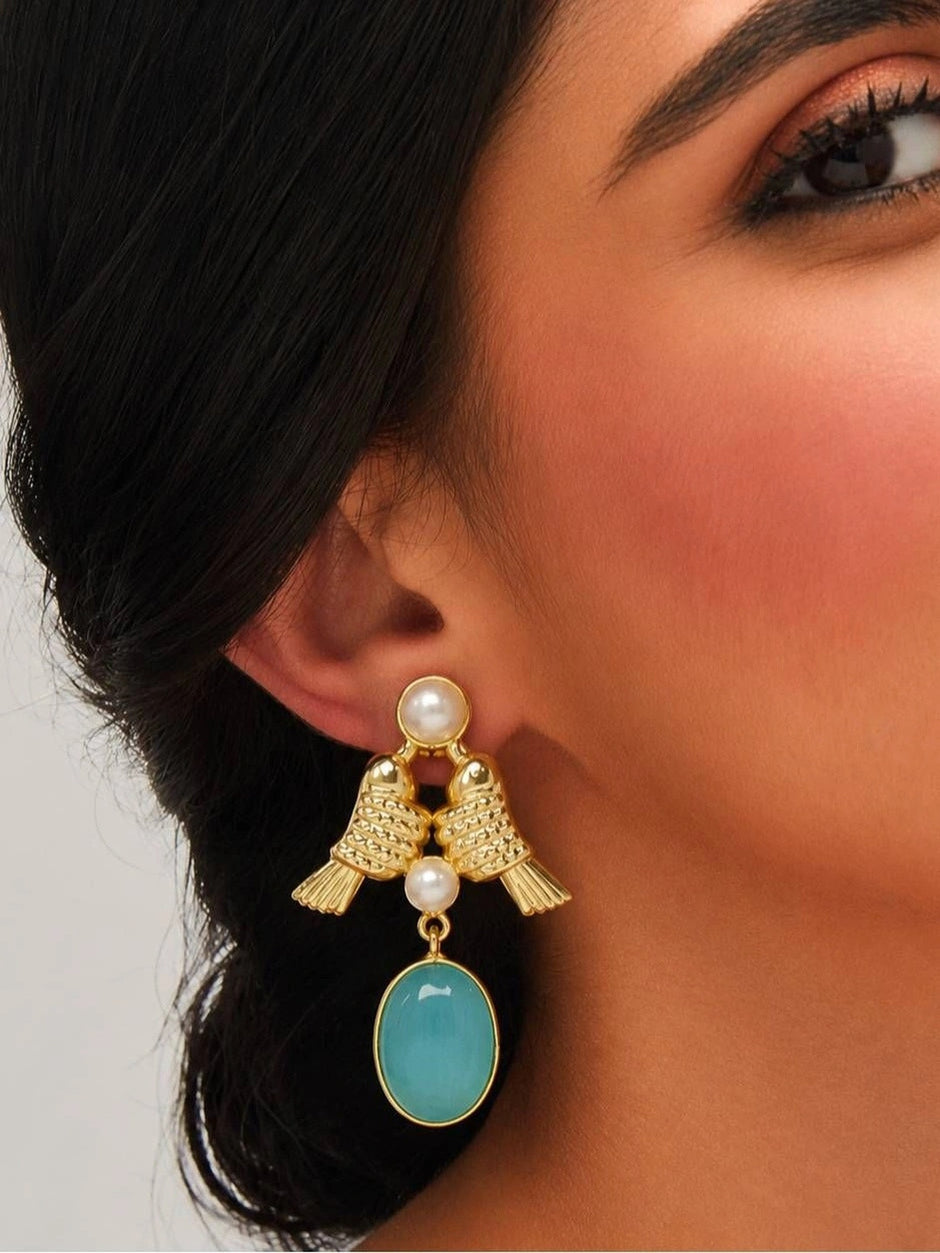Close-up of gold lovebird and aqua cat-eye drop earring worn on a woman's ear