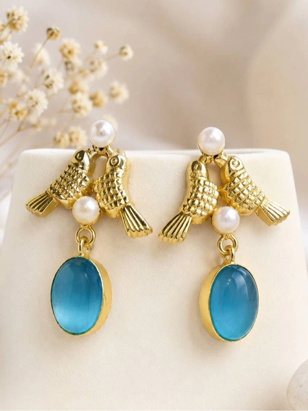 Pair of gold-plated lovebird earrings with teal oval stone drops displayed on white surface