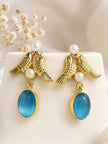 Pair of gold-plated lovebird earrings with teal oval stone drops displayed on white surface