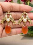 Close-up of two gold love birds earrings with pearl and carnelian resin drops resting on a hand