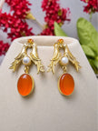 Gold-plated bird motif drop earrings displayed on a beige jewellery stand with red flowers in background