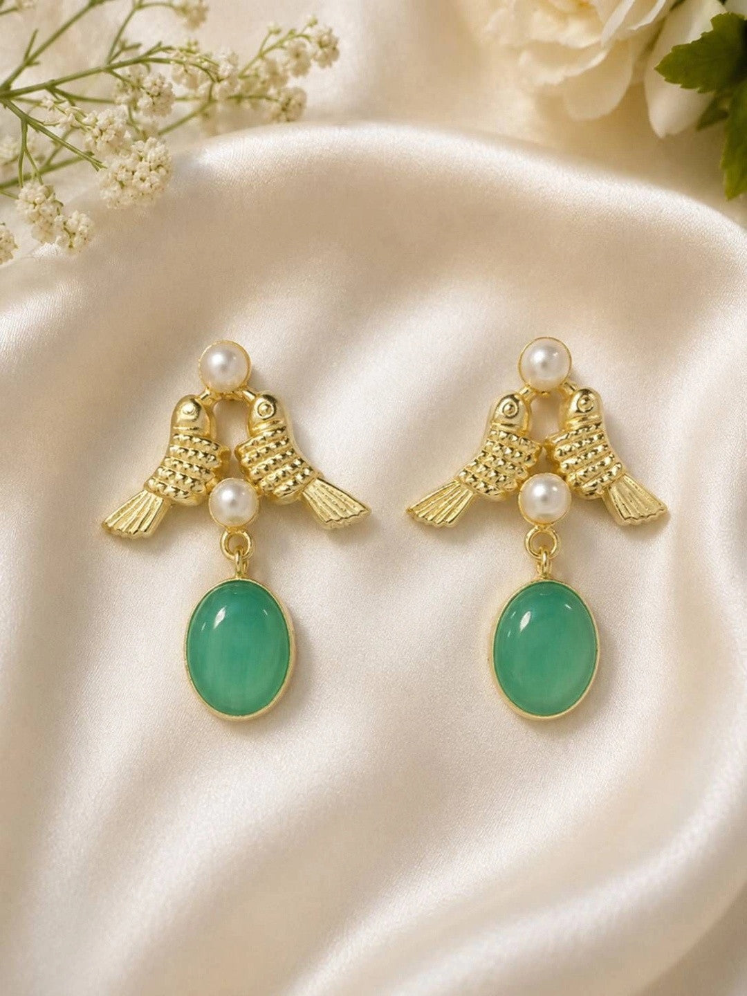 Pair of gold-plated twin bird drop earrings with pearl beads and oval green stone pendants on cream satin fabric