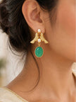 Gold-plated twin bird earring with green stone drop worn on a woman's ear against a soft blurred background