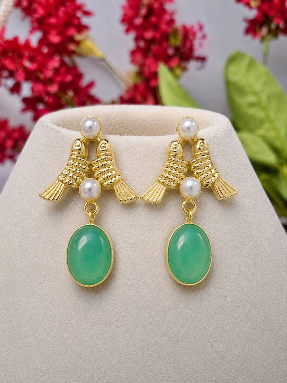 Both gold-plated bird drop earrings displayed upright on a beige jewellery stand with red flowers behind