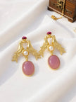 Pair of gold-plated love bird drop earrings with pink oval cabochon and pearl accent on white fabric