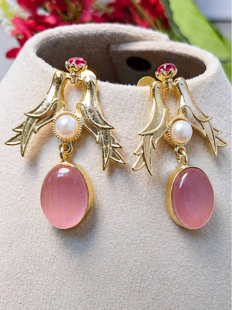 Close-up of gold bird motif earrings with pink stone drops displayed on a beige jewellery stand