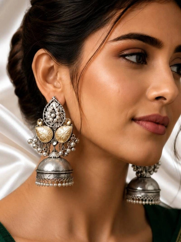 Woman wearing large oxidised silver kundan jhumka earrings with pearl fringe against a white drape