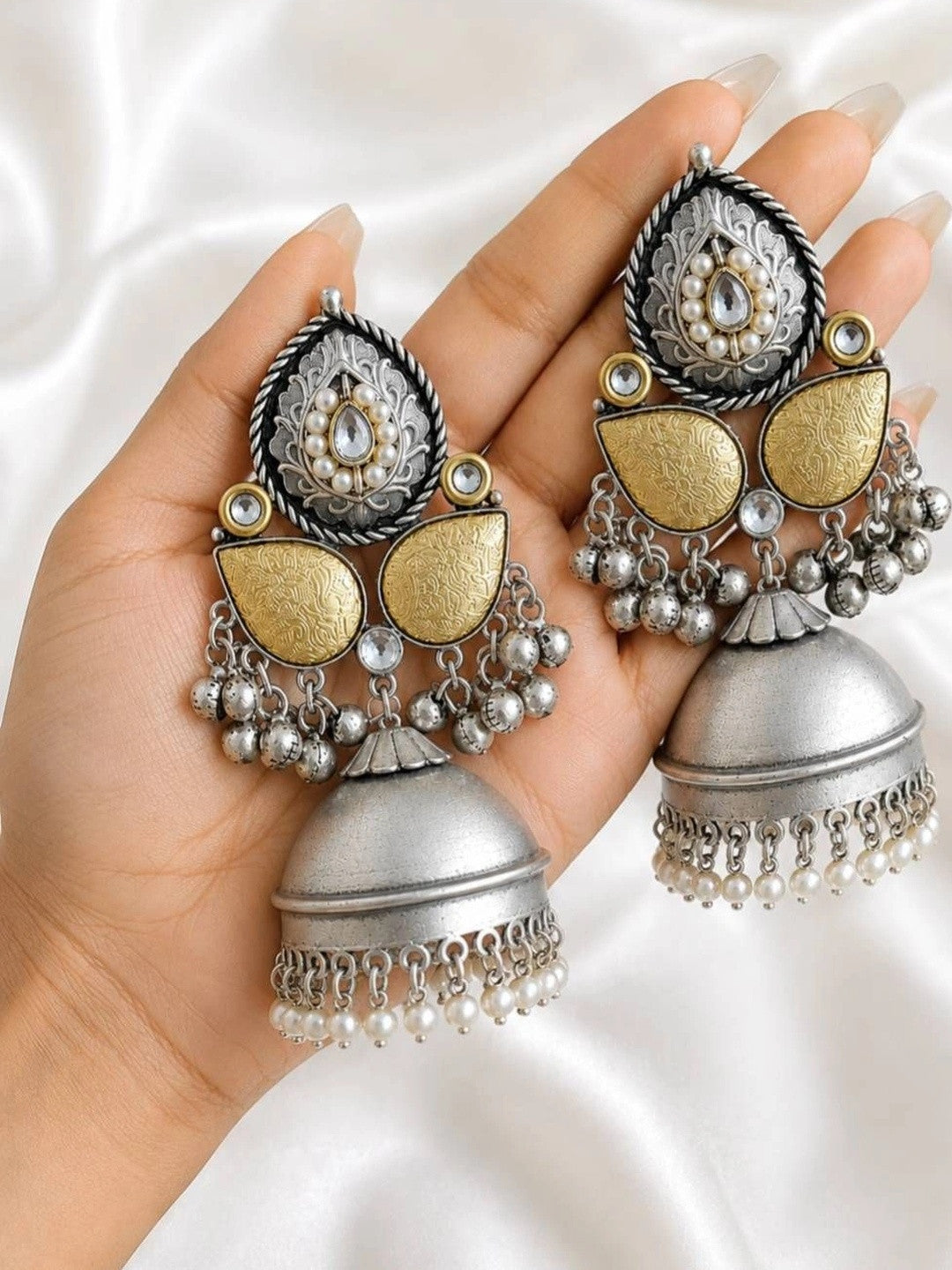 Two oxidised silver jhumka earrings resting on an open palm showing full length and gold-tone panels