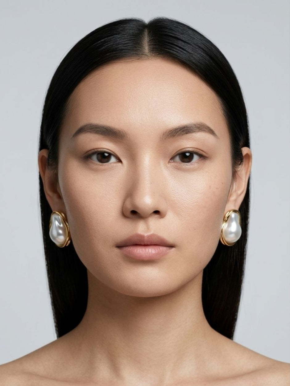 Model facing forward wearing gold baroque pearl stud earrings on both ears