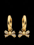 Pair of gold-plated huggie hoop earrings with pavé cubic zirconia bow charms on black background