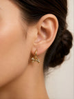 Close-up of gold bow charm hoop earring worn on a woman with dark hair in a bun