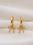 Close-up of two gold bow charm hoop earrings resting on white cloth showing beaded bow detail