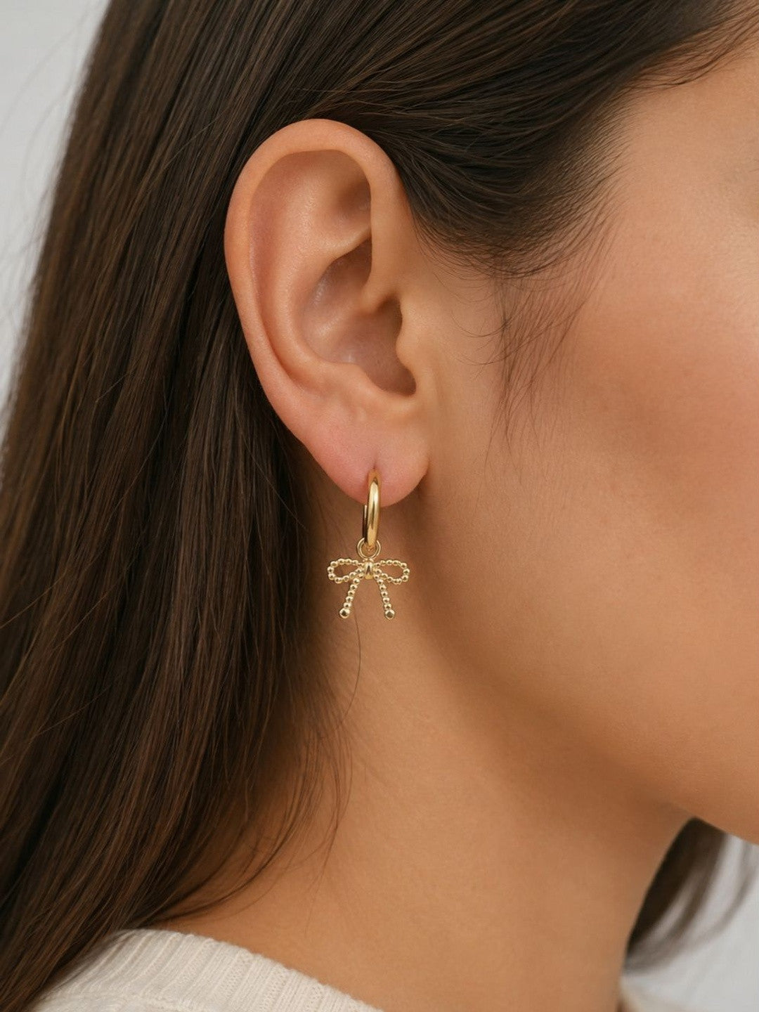Side profile of a woman wearing a gold hoop earring with a beaded bow charm pendant