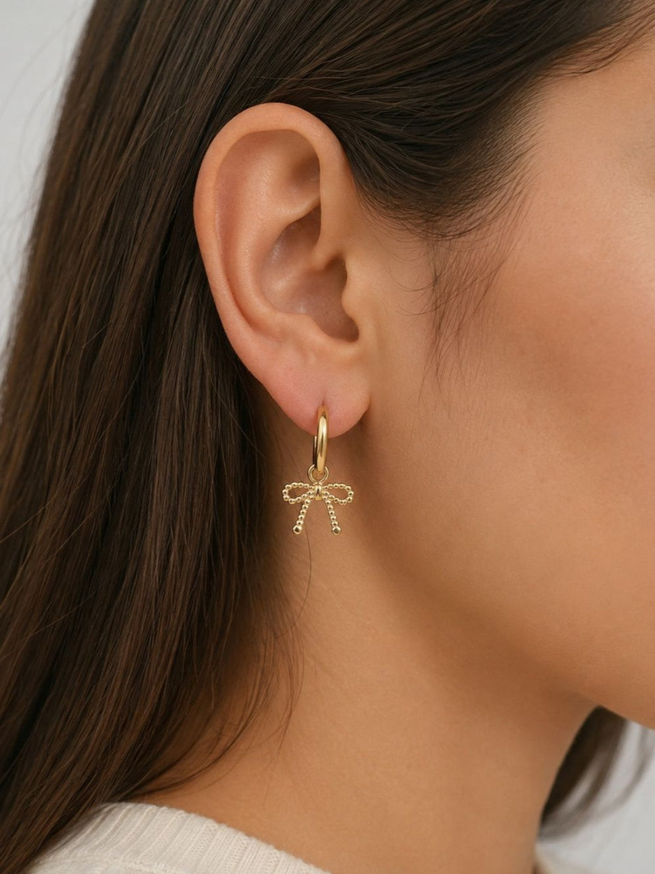 Side profile of a woman wearing a gold hoop earring with a beaded bow charm pendant