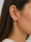 Side profile of a woman wearing a gold hoop earring with a beaded bow charm pendant