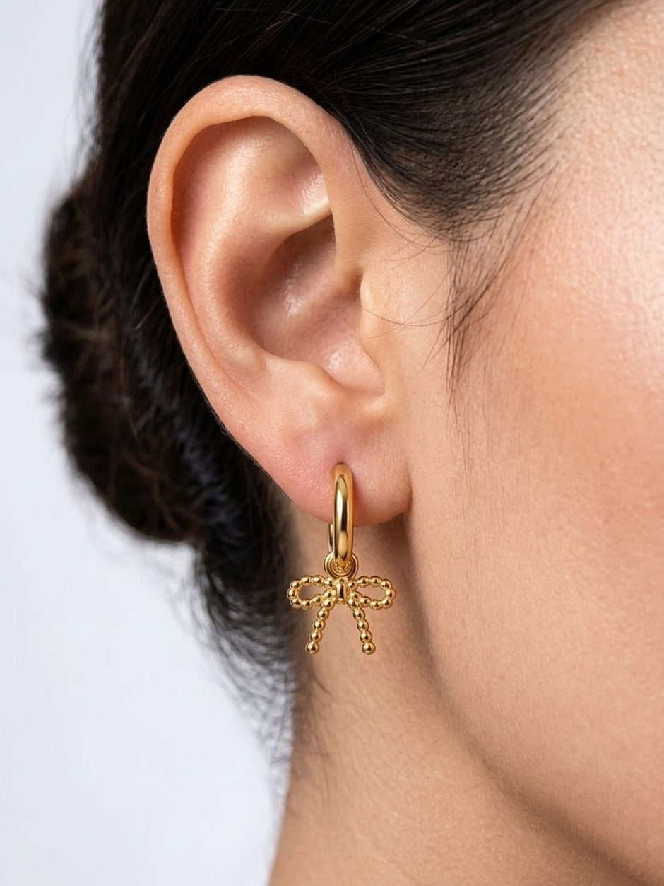 Close-up rear-angle view of gold beaded bow charm hoop earring worn on a woman's ear