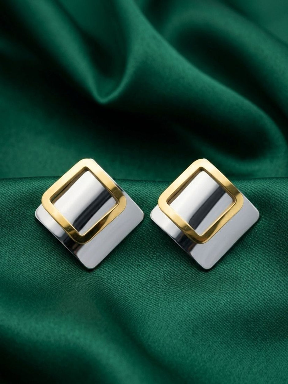 Pair of two-tone square stud earrings with gold-finish open frame on silver base, displayed on green satin fabric