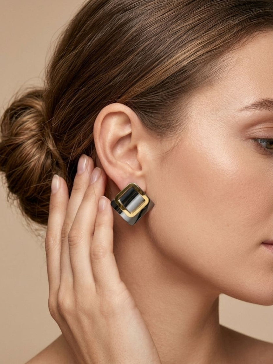Close-up of a woman wearing a two-tone square stud earring showing gold open frame over polished silver base