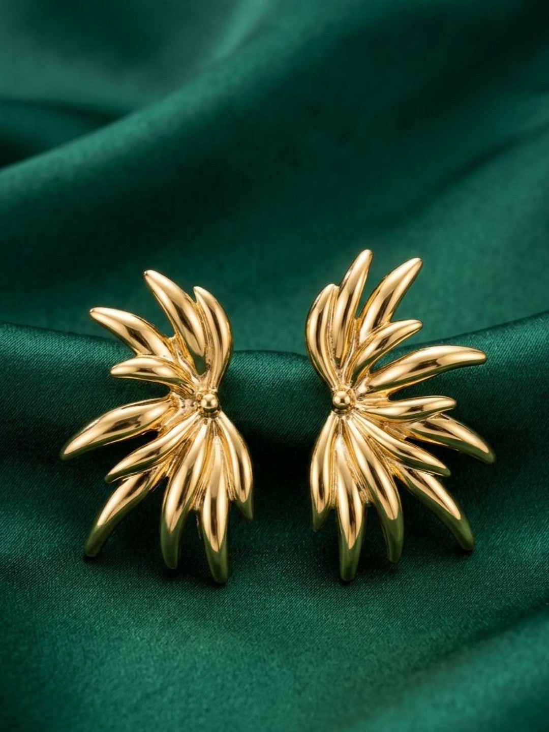 Pair of gold-plated floral burst stud earrings displayed on deep green satin fabric