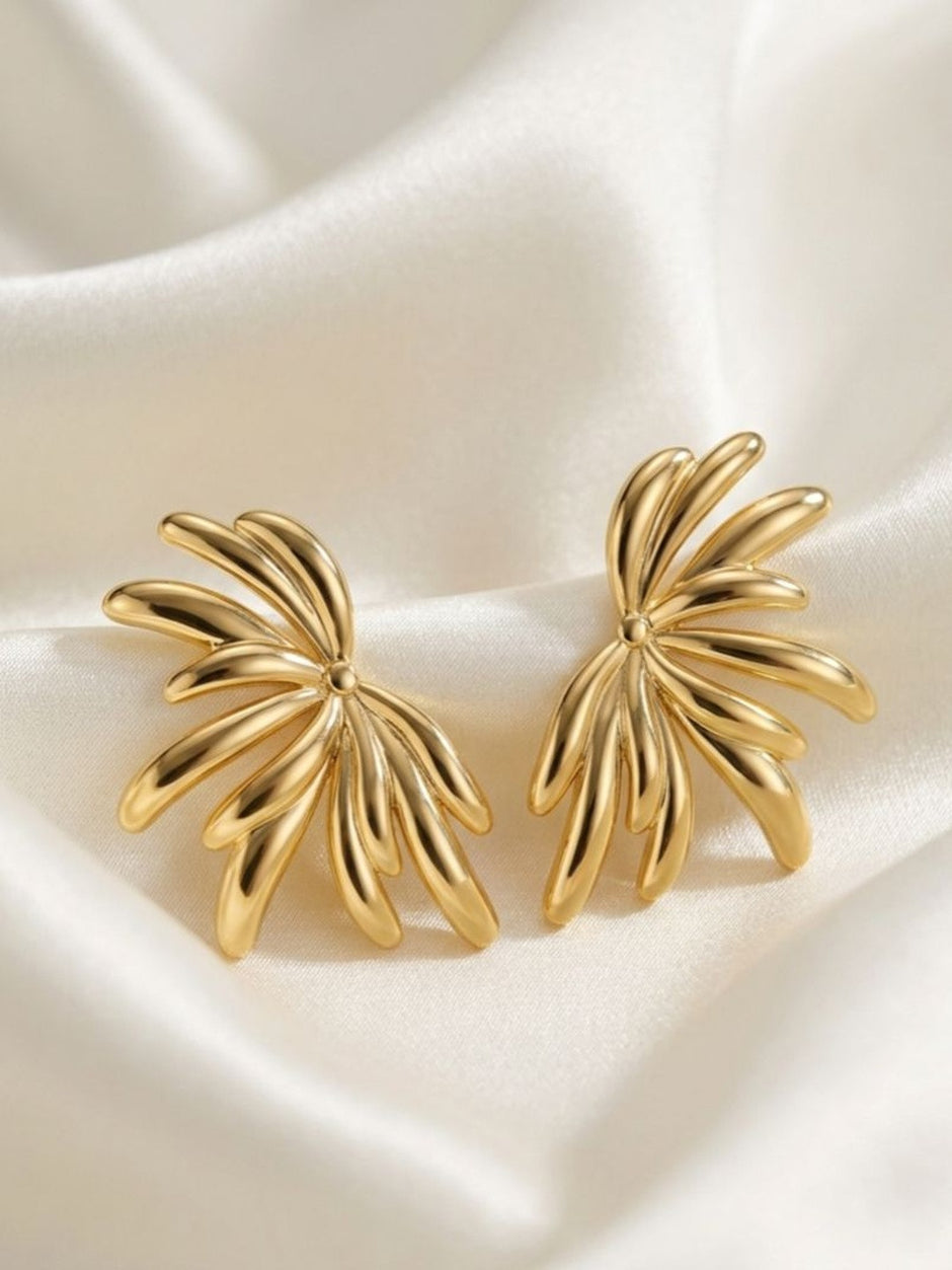 Two gold-plated radiating petal stud earrings laid flat on white satin cloth