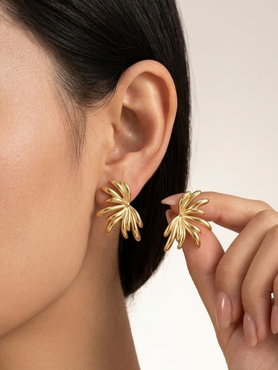 Close-up of woman wearing gold floral stud earring on left ear, holding second earring