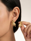 Close-up of woman wearing gold floral stud earring on left ear, holding second earring