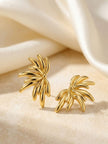 Pair of gold-plated floral stud earrings resting on cream textured fabric surface