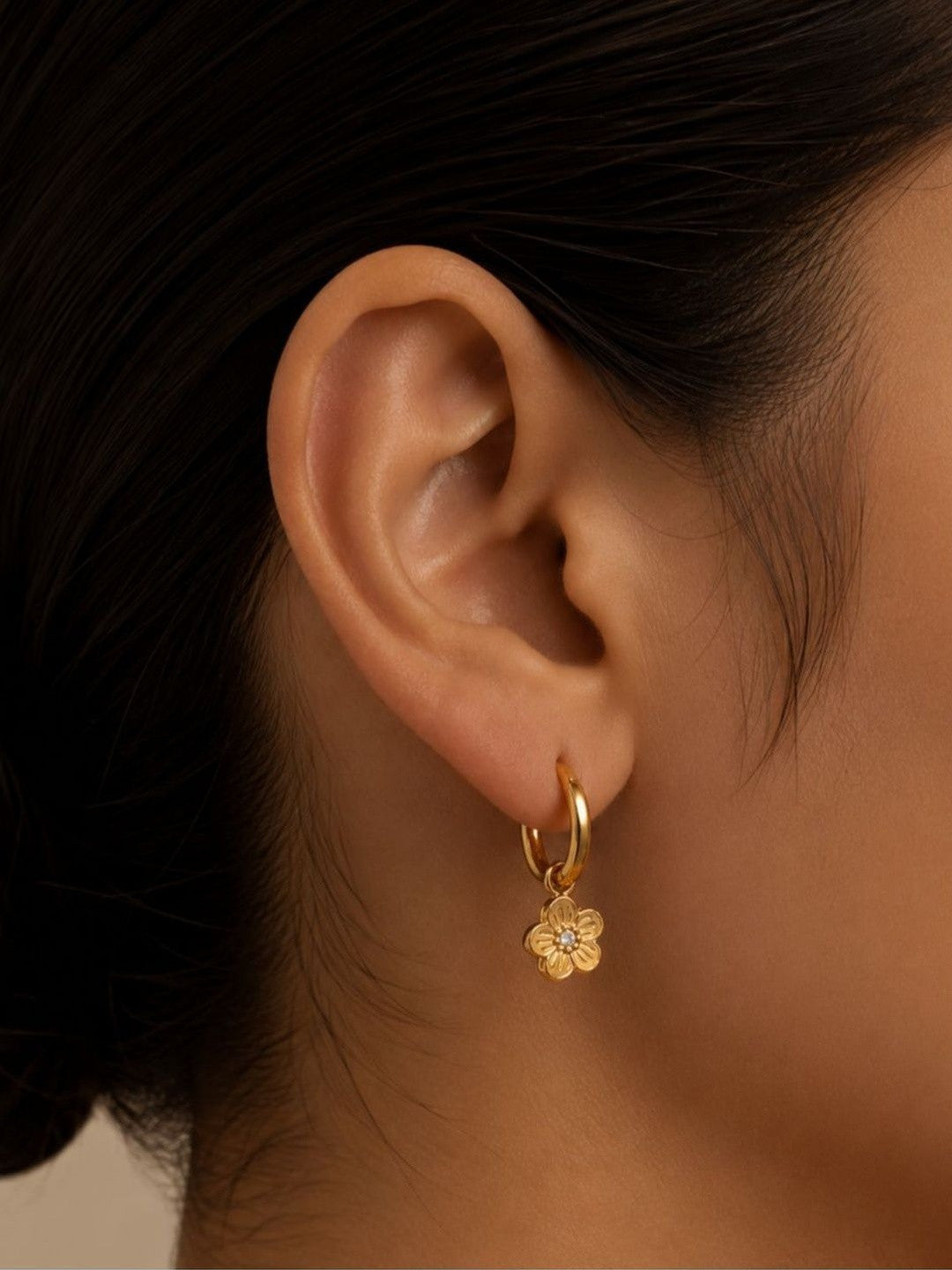 Gold flower charm hoop earring worn on a model's ear showing size and fit