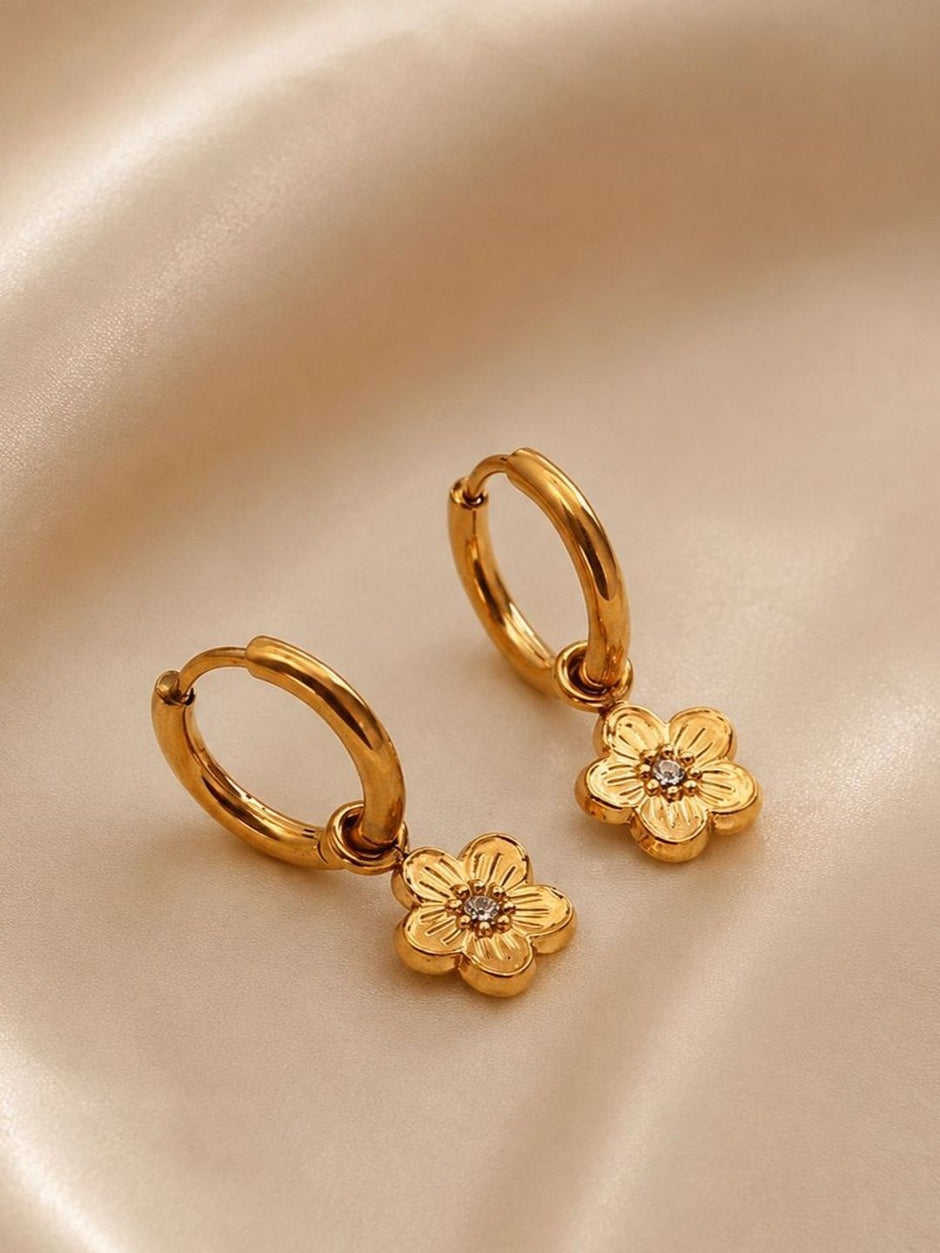 Close-up of gold flower charm hoops on satin showing engraved petal detail and crystal centre
