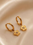 Close-up of gold flower charm hoops on satin showing engraved petal detail and crystal centre