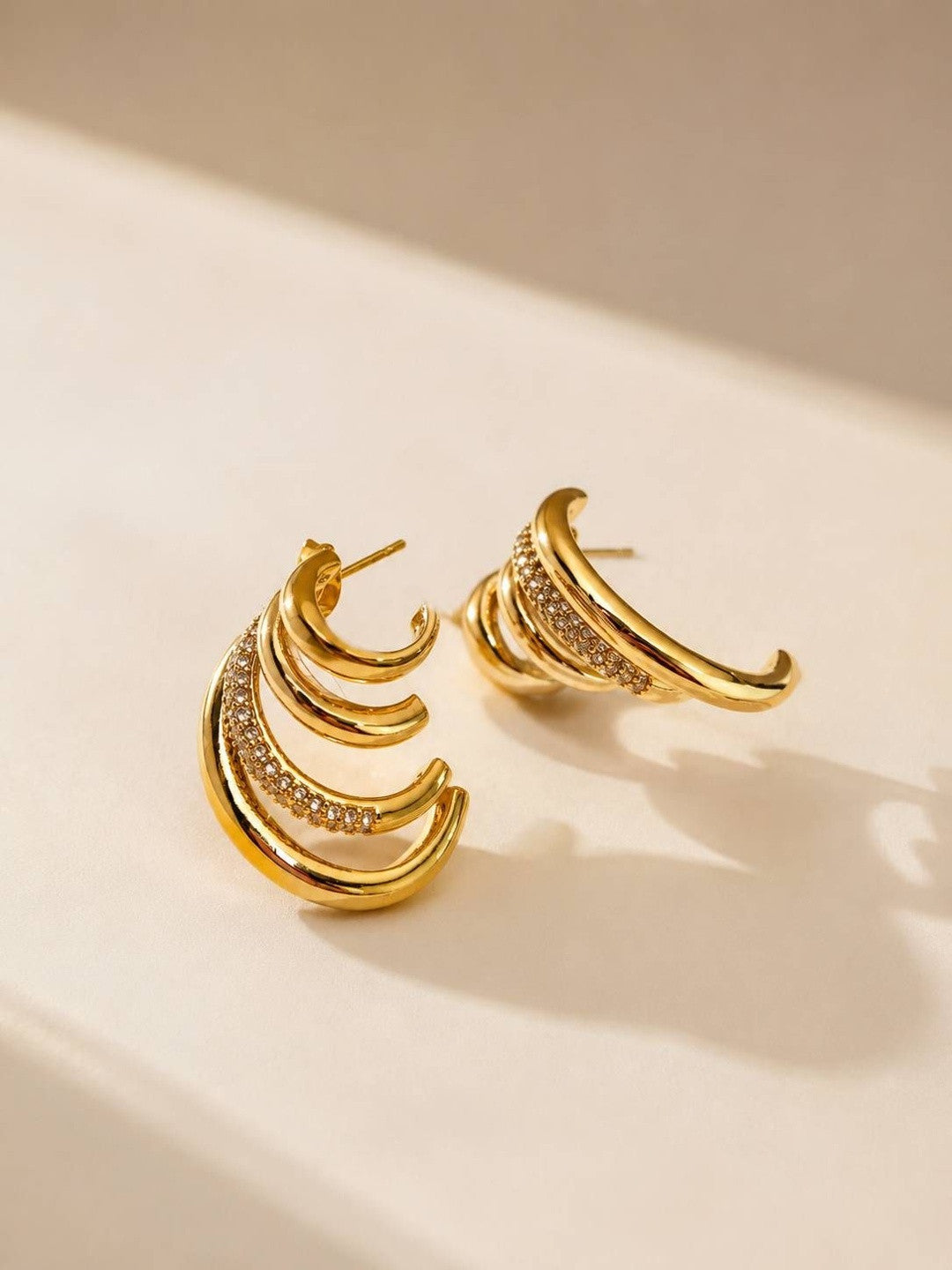 Two gold layered hoop earrings lying flat on a cream surface showing graduated band detail