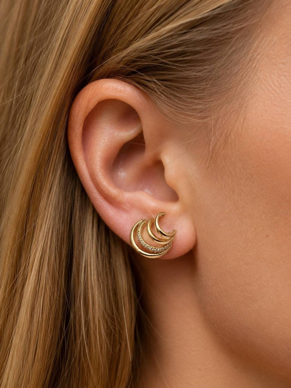 Gold triple-hoop earring worn on model with blonde hair showing front-facing crescent silhouette