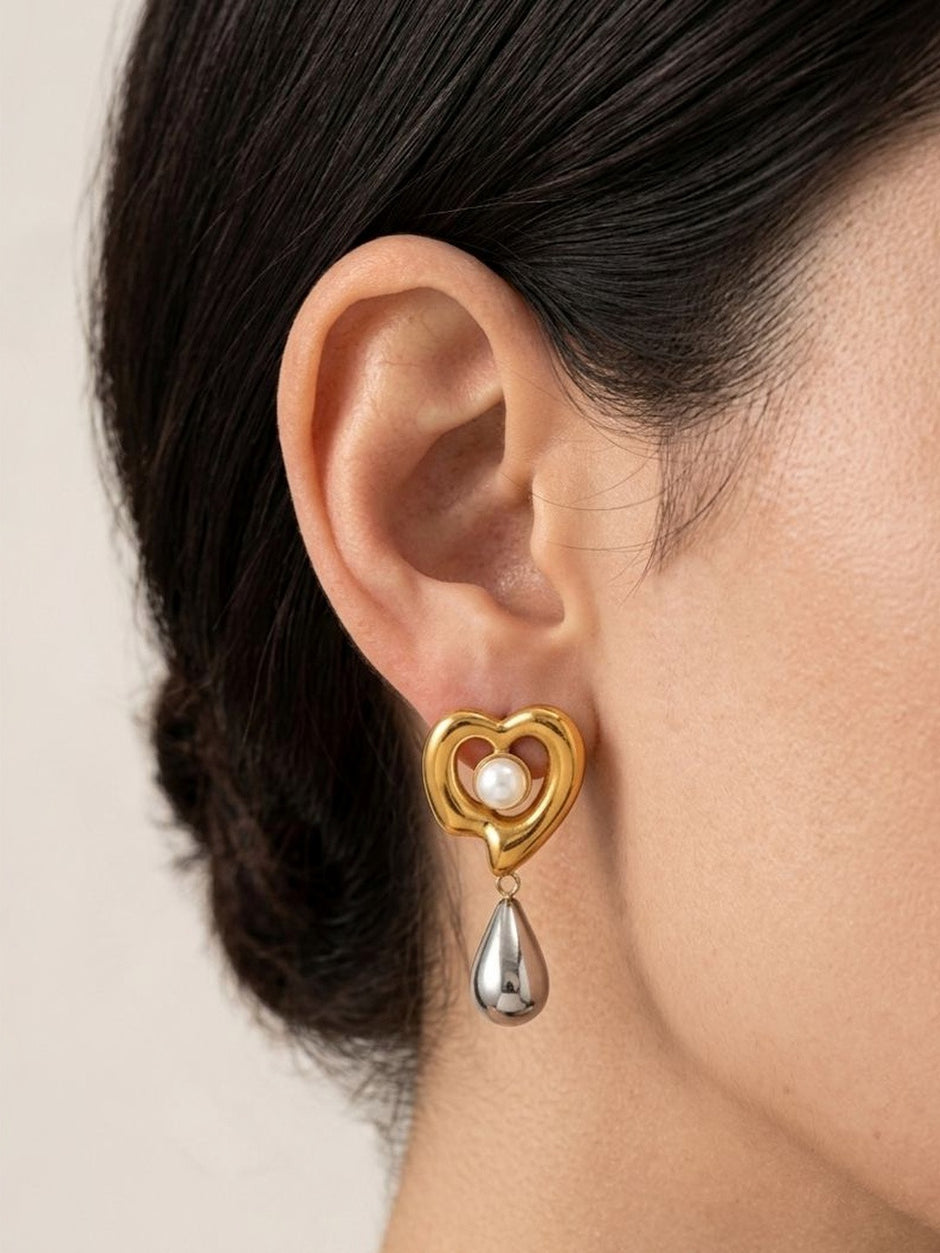 Model wearing gold-tone heart drop earring with silver teardrop pendant on left ear