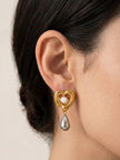 Model wearing gold-tone heart drop earring with silver teardrop pendant on left ear