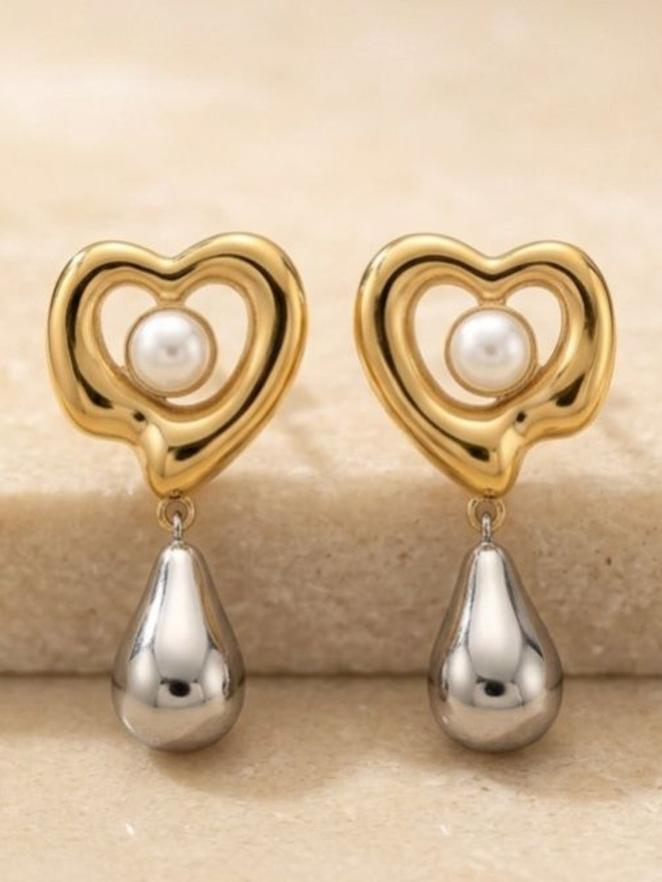 Close-up of two gold heart earrings with faux pearl and silver teardrop on stone surface