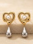 Close-up of two gold heart earrings with faux pearl and silver teardrop on stone surface