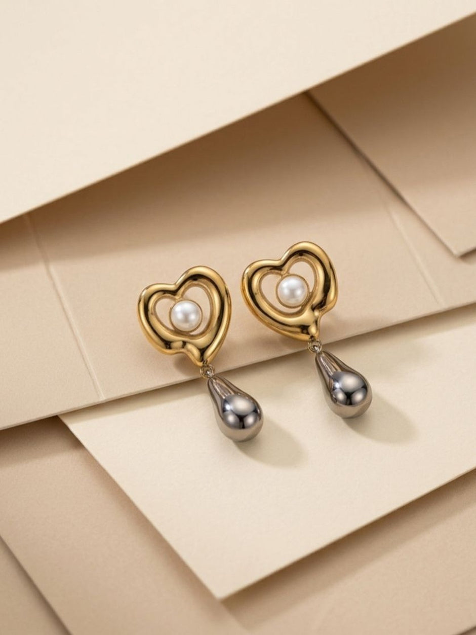 Gold heart drop earrings with silver teardrop pendants displayed on layered beige paper background