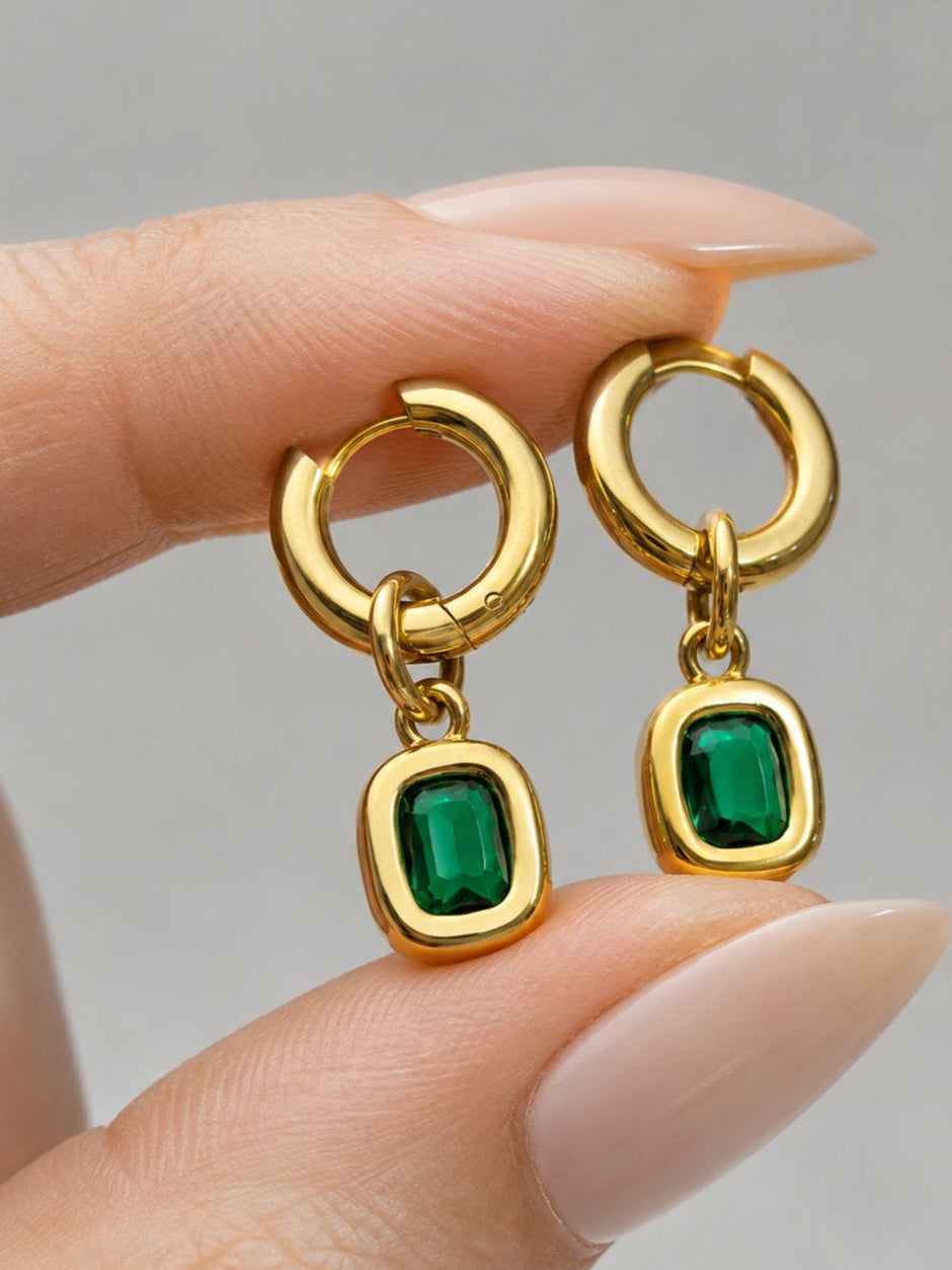 Close-up of gold-plated emerald drop hoop earrings held between fingers showing stone detail and hoop clasp